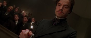 Movie still from “From Hell” (2001), directed by Allen Hughes – A man in a suit and tie holding a glass of wine; Close Up shot, Low angle