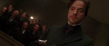 Movie still from “From Hell” (2001), directed by Allen Hughes – A man in a suit and tie holding a glass of wine; Close Up shot, Low angle