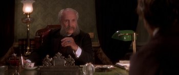 Movie still from “From Hell” (2001), directed by Allen Hughes – An older man sitting at a desk in front of a green lamp; Close Up shot, Low angle
