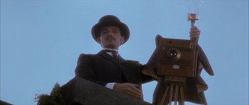 Movie still from “From Hell” (2001), directed by Allen Hughes – A man in a suit and hat holding an old fashioned camera; Close Up shot, Low angle