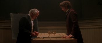 Movie still from “From Hell” (2001), directed by Allen Hughes – Two men in suits are looking at an object on a table; Medium shot, High angle