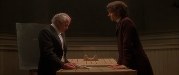 Movie still from “From Hell” (2001), directed by Allen Hughes – Two men are sitting at a table and one of the men is holding a pair of scissors; Medium shot, High angle