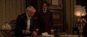 Movie still from “From Hell” (2001), directed by Allen Hughes – A man in a suit and tie standing next to another man in a suit and tie; Medium shot, High angle