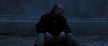 Movie still from “From Hell” (2001), directed by Allen Hughes – A man sitting on the ground in the dark; Medium shot, Low angle