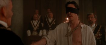 Movie still from “From Hell” (2001), directed by Allen Hughes – A blindfolded man standing in front of a group of people; Close Up shot, Over the shoulder angle