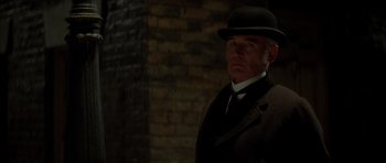 Movie still from “From Hell” (2001), directed by Allen Hughes – A man wearing a suit and hat in a dimly - lit room; Medium shot, Low angle