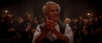 Movie still from “From Hell” (2001), directed by Allen Hughes – An old man clasping his hands in front of a crowd; Close Up shot, High angle