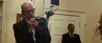 Movie still from “Frost/Nixon” (2008), directed by Ron Howard – An older man taking a picture with a camera in front of another man; Close Up shot, Low angle