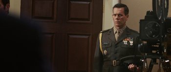 Movie still from “Frost/Nixon” (2008), directed by Ron Howard – A man in a military uniform standing in front of a door; Medium shot, Low angle
