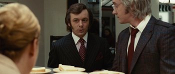 Movie still from “Frost/Nixon” (2008), directed by Ron Howard – A man wearing a suit and tie standing next to a table; Close Up shot, Over the shoulder angle