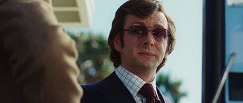 Movie still from “Frost/Nixon” (2008), directed by Ron Howard – A person wearing a suit and sunglasses; Close Up shot, Over the shoulder angle
