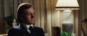 Movie still from “Frost/Nixon” (2008), directed by Ron Howard – A man wearing a suit and tie in front of a lamp; Close Up shot, Over the shoulder angle