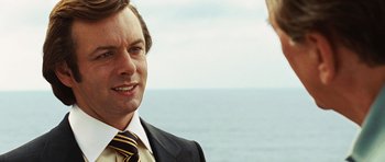 Movie still from “Frost/Nixon” (2008), directed by Ron Howard – A man wearing a suit and tie standing next to another man wearing a suit; Close Up shot, Over the shoulder angle