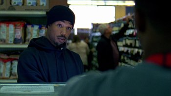 Movie still from “Fruitvale Station” (2013), directed by Ryan Coogler – A man in a black jacket and a black hat is in a store; Close Up shot, Over the shoulder angle