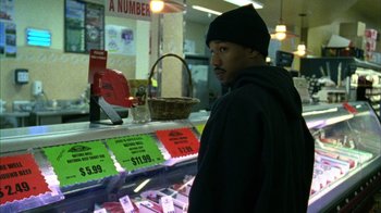 Movie still from “Fruitvale Station” (2013), directed by Ryan Coogler – A man standing in front of a display of meat; Medium shot, High angle