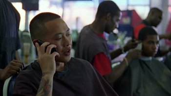 Movie still from “Fruitvale Station” (2013), directed by Ryan Coogler – A man talking on a cell phone while sitting in a barber shop; Close Up shot, Over the shoulder angle