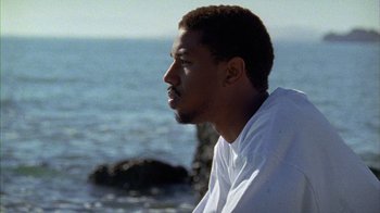 Movie still from “Fruitvale Station” (2013), directed by Ryan Coogler – A man looking out at the ocean while sitting on a bench; Close Up shot, Low angle