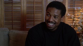 Movie still from “Fruitvale Station” (2013), directed by Ryan Coogler – A man sitting on a couch smiling for the camera; Close Up shot, Over the shoulder angle