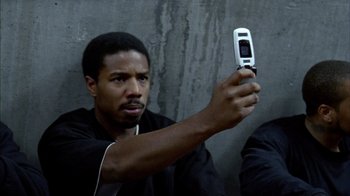 Movie still from “Fruitvale Station” (2013), directed by Ryan Coogler – A man holding up a cell phone to take a picture; Close Up shot, Low angle