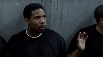 Movie still from “Fruitvale Station” (2013), directed by Ryan Coogler – A man in black shirt talking to someone in front of a gray wall; Close Up shot, Over the shoulder angle