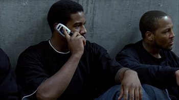 Movie still from “Fruitvale Station” (2013), directed by Ryan Coogler – A man talking on a cell phone next to another man; Medium shot, Low angle