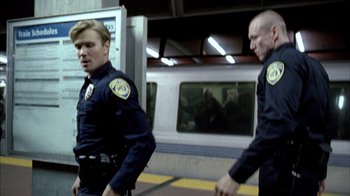 Movie still from “Fruitvale Station” (2013), directed by Ryan Coogler – Two police officers standing next to each other on a train platform; Medium shot, Over the shoulder angle