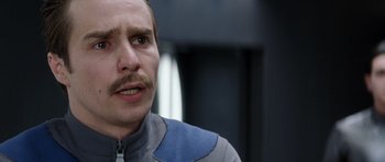 Movie still from “Galaxy Quest” (1999), directed by Dean Parisot – A person with a mustache wearing a suit; Close Up shot, Over the shoulder angle