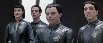 Movie still from “Galaxy Quest” (1999), directed by Dean Parisot – A man in a black and silver suit is standing next to another man in a black and silver suit; Close Up shot, Over the shoulder angle