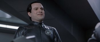Movie still from “Galaxy Quest” (1999), directed by Dean Parisot – A man wearing a black suit and smiling for the camera; Close Up shot, Over the shoulder angle