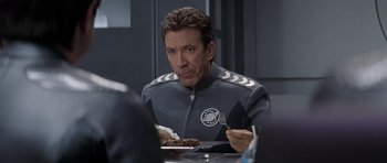 Movie still from “Galaxy Quest” (1999), directed by Dean Parisot – A man in a space suit sitting in front of a plate of food; Close Up shot, Over the shoulder angle