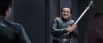Movie still from “Galaxy Quest” (1999), directed by Dean Parisot – A man in a black leather jacket holding a baseball bat; Medium shot, Over the shoulder angle