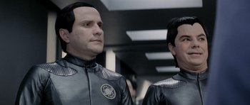 Movie still from “Galaxy Quest” (1999), directed by Dean Parisot – Two men in black and silver suits standing next to each other; Close Up shot, Over the shoulder angle