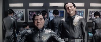 Movie still from “Galaxy Quest” (1999), directed by Dean Parisot – Two men dressed in black suits smiling for the camera; Medium shot, Over the shoulder angle