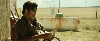 Movie still from “Hell or High Water” (2016), directed by David Mackenzie – A man sitting on the ground holding a leaf in his hand; Medium shot, Over the shoulder angle