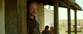 Movie still from “Hell or High Water” (2016), directed by David Mackenzie – A man standing next to another man on a porch; Medium shot, Low angle