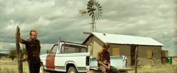 Movie still from “Hell or High Water” (2016), directed by David Mackenzie – A man sitting on the back of a truck in front of a windmill; Wide shot, Low angle