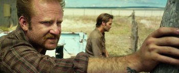 Movie still from “Hell or High Water” (2016), directed by David Mackenzie – Two men sitting in the grass near a fence; Close Up shot, Over the shoulder angle