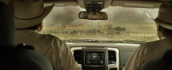 Movie still from “Hell or High Water” (2016), directed by David Mackenzie – A herd of wild animals in a field with smoke coming out of the sky; Wide shot, Over the shoulder angle