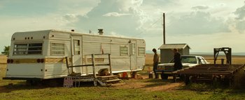 Movie still from “Hell or High Water” (2016), directed by David Mackenzie – A man standing in front of an old trailer; Extreme Wide shot, Low angle