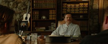 Movie still from “Hell or High Water” (2016), directed by David Mackenzie – A man sitting at a desk in front of a book case; Medium shot, Low angle