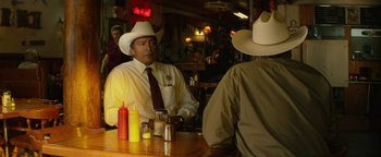 Movie still from “Hell or High Water” (2016), directed by David Mackenzie – A man sitting at a table in a cowboy hat; Medium shot, Over the shoulder angle