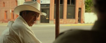 Movie still from “Hell or High Water” (2016), directed by David Mackenzie – A man wearing a white hat sitting on the side of the street; Medium shot, Over the shoulder angle