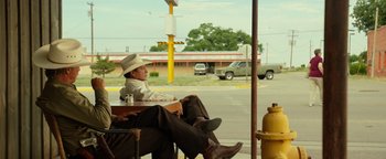 Movie still from “Hell or High Water” (2016), directed by David Mackenzie – A man sitting at a table with his feet on the ground; Wide shot, Over the shoulder angle