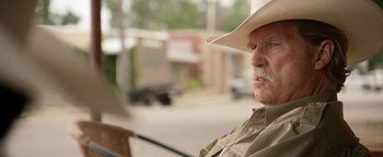 Movie still from “Hell or High Water” (2016), directed by David Mackenzie – An older man wearing a cowboy hat sitting on a bench; Close Up shot, Over the shoulder angle