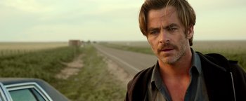 Movie still from “Hell or High Water” (2016), directed by David Mackenzie – A man standing on the side of a road near a field; Close Up shot, Over the shoulder angle