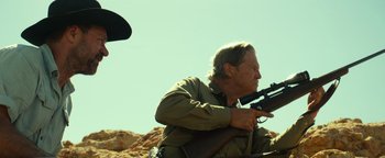Movie still from “Hell or High Water” (2016), directed by David Mackenzie – A man holding a gun while standing on a hill; Medium shot, Low angle