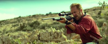 Movie still from “Hell or High Water” (2016), directed by David Mackenzie – A man is holding a rifle and aiming with a scope; Medium shot, Over the shoulder angle