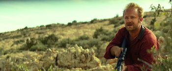 Movie still from “Hell or High Water” (2016), directed by David Mackenzie – A man holding a rifle in a field; Medium shot, Over the shoulder angle