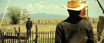 Movie still from “Hell or High Water” (2016), directed by David Mackenzie – A man wearing a cowboy hat standing next to a fence; Extreme Wide shot, Over the shoulder angle