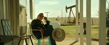 Movie still from “Hell or High Water” (2016), directed by David Mackenzie – A man sitting on a chair in front of an oil well; Medium shot, Low angle
